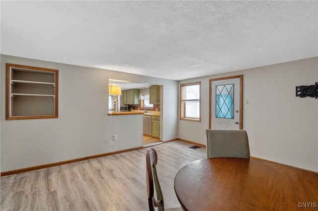 unfurnished dining area featuring visible vents, a sink, a textured ceiling, light wood-type flooring, and baseboards