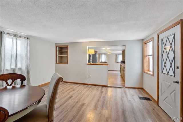 dining room featuring a textured ceiling, light wood-type flooring, visible vents, and baseboards