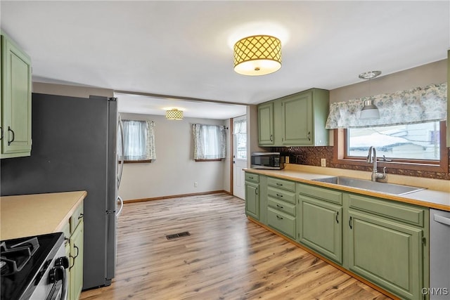 kitchen featuring stainless steel appliances, a sink, light wood-style flooring, and green cabinetry