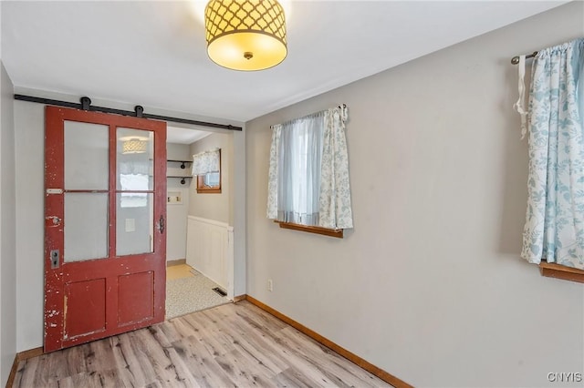 entrance foyer featuring a barn door, light wood-style flooring, and baseboards