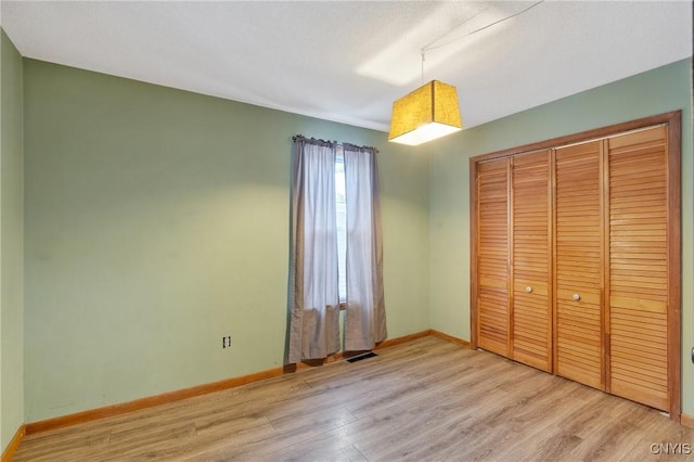 unfurnished bedroom featuring a closet, visible vents, light wood-style flooring, and baseboards