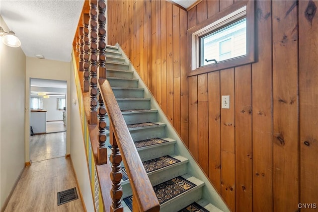 staircase with wood walls, visible vents, and wood finished floors