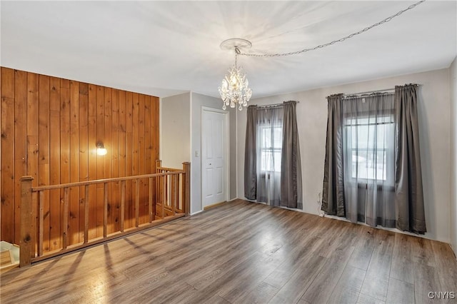 empty room with an inviting chandelier, wood finished floors, and wood walls