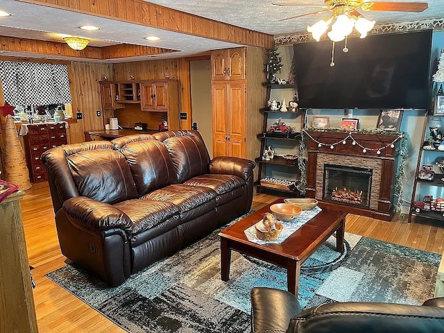 living area with light wood finished floors, ceiling fan, a textured ceiling, wood walls, and a fireplace