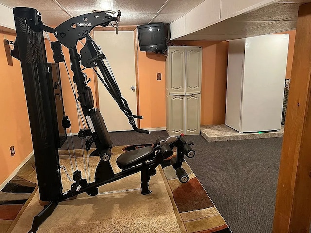 workout room featuring a paneled ceiling and baseboards