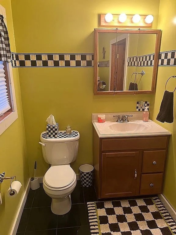 half bathroom featuring toilet, baseboards, and vanity