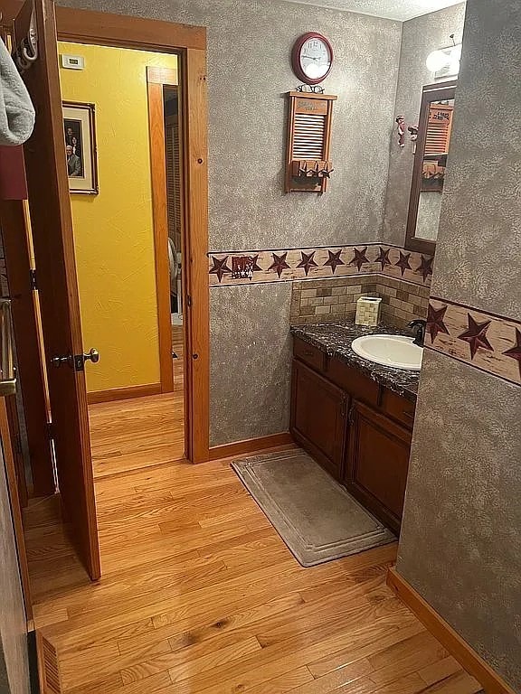 bathroom with wallpapered walls, wood finished floors, vanity, and baseboards