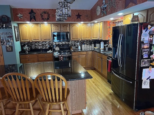 kitchen featuring dark countertops, black appliances, light wood-style flooring, and a breakfast bar area