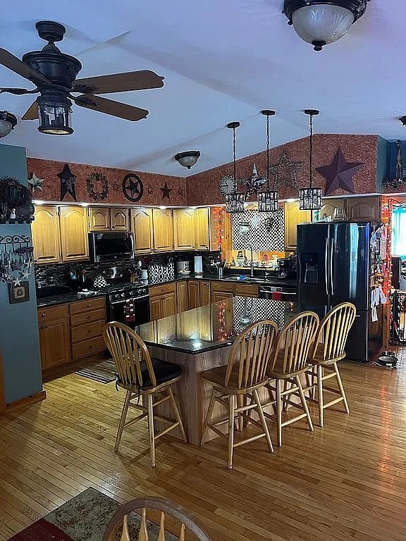 kitchen with vaulted ceiling, black appliances, dark countertops, and light wood-style floors