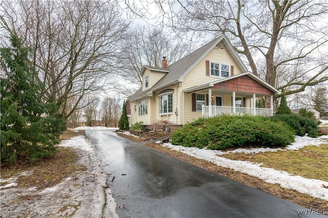 view of front of property featuring driveway, a porch, and a chimney