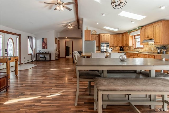 dining space with a ceiling fan, vaulted ceiling with skylight, dark wood finished floors, and baseboard heating