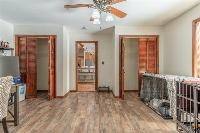 bedroom with ceiling fan, baseboards, two closets, and wood finished floors