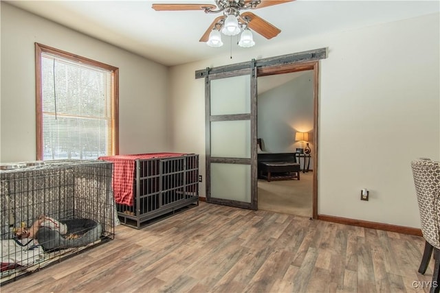 interior space featuring a barn door, wood finished floors, a ceiling fan, and baseboards