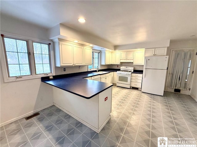 kitchen with white appliances, visible vents, dark countertops, a peninsula, and under cabinet range hood