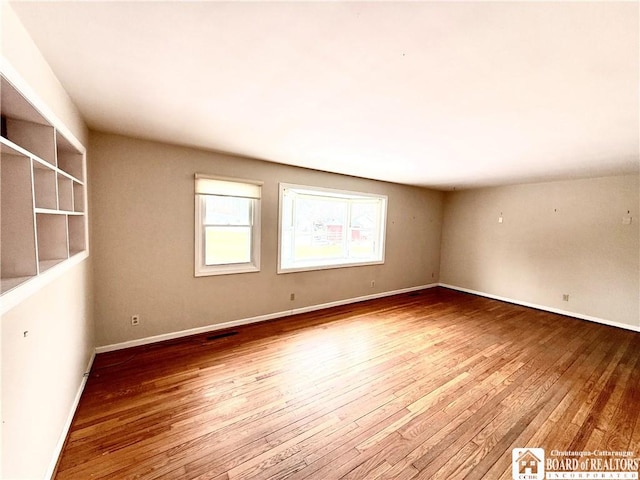 empty room featuring baseboards, visible vents, and hardwood / wood-style floors