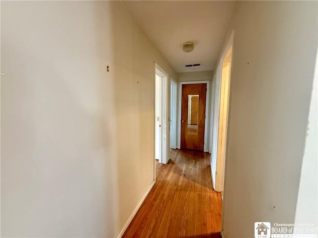 hall featuring baseboards, visible vents, and light wood finished floors