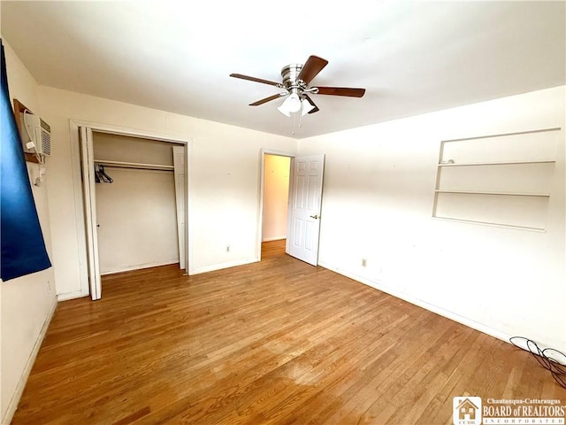 unfurnished bedroom with a closet, a wall mounted AC, a ceiling fan, wood finished floors, and baseboards