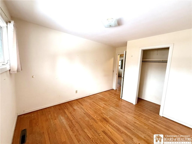 unfurnished bedroom with a closet, light wood-type flooring, visible vents, and baseboards