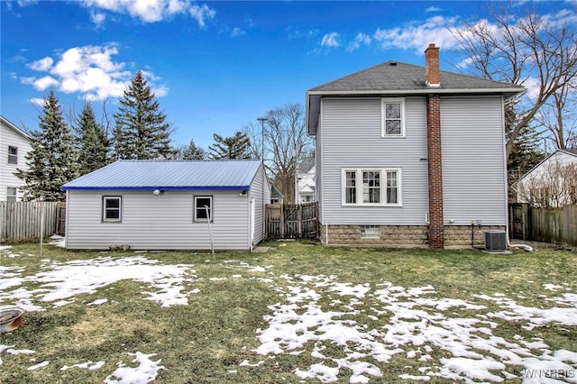 snow covered house featuring an outbuilding, central AC, a chimney, and a fenced backyard