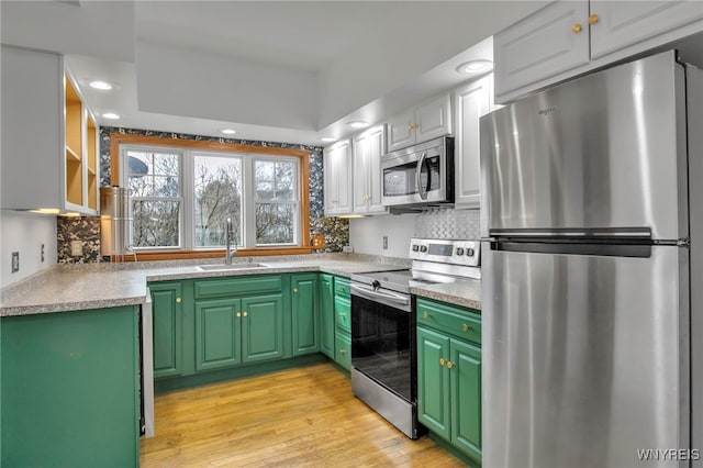 kitchen featuring decorative backsplash, light wood-style flooring, appliances with stainless steel finishes, green cabinets, and a sink