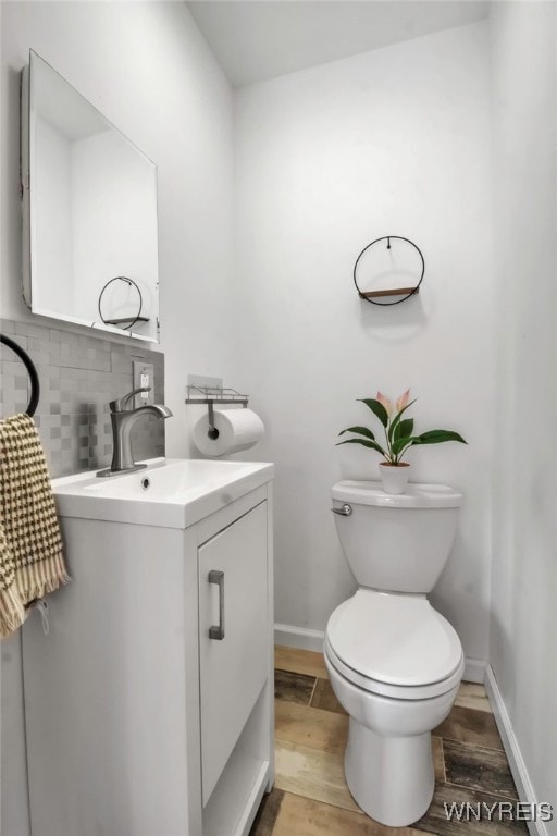 bathroom featuring baseboards, decorative backsplash, toilet, wood finished floors, and vanity