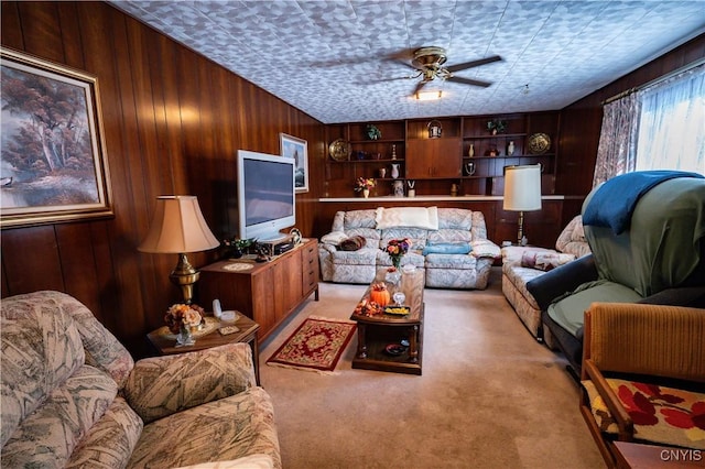 living area with a ceiling fan, light colored carpet, and wood walls