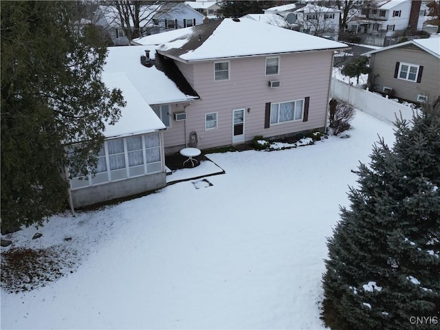 snow covered property featuring a sunroom, fence, and an AC wall unit