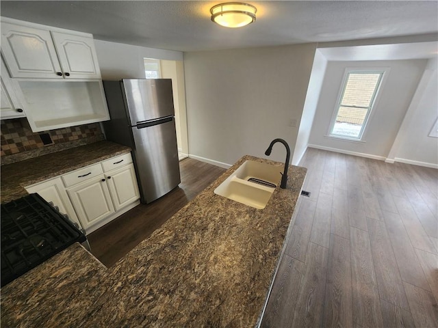 kitchen featuring dark wood-style flooring, decorative backsplash, freestanding refrigerator, white cabinets, and a sink