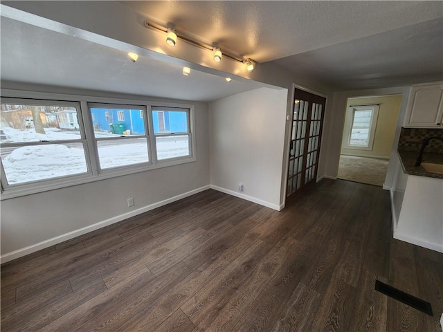 unfurnished living room with dark wood-style flooring, a sink, and baseboards