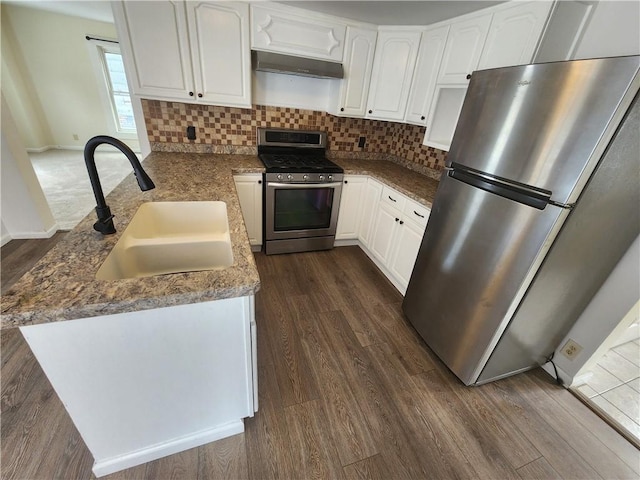 kitchen with dark wood-type flooring, a peninsula, stainless steel appliances, under cabinet range hood, and a sink