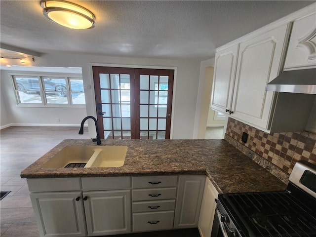 kitchen featuring white cabinets, dark stone countertops, a sink, stainless steel gas range, and backsplash