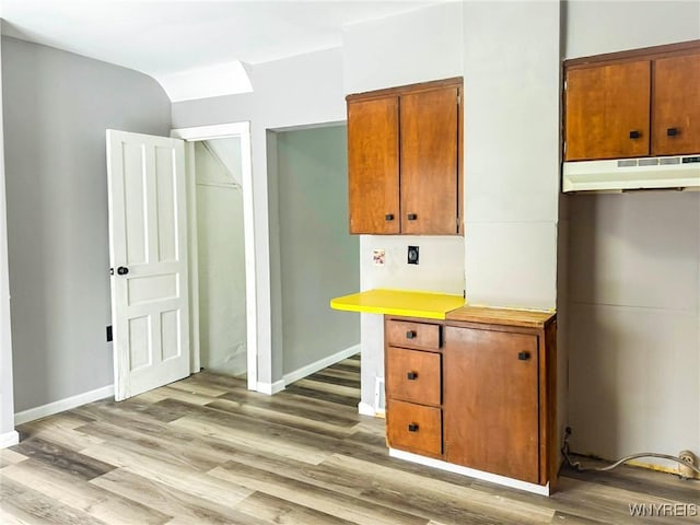 kitchen featuring light wood-style floors, light countertops, brown cabinets, and under cabinet range hood