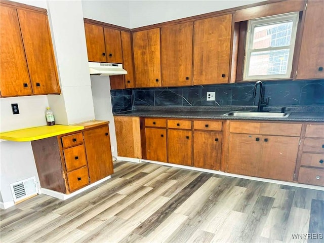 kitchen with visible vents, light wood-style flooring, backsplash, a sink, and under cabinet range hood