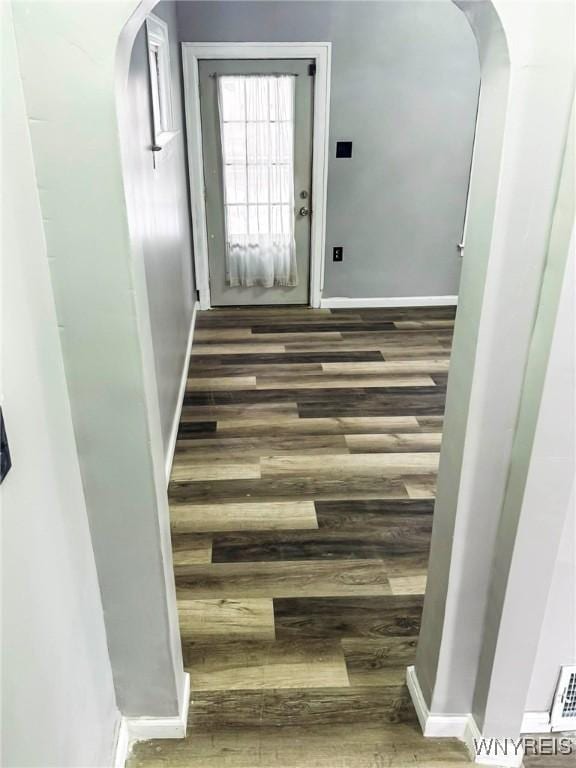 hallway featuring baseboards, arched walkways, and wood finished floors