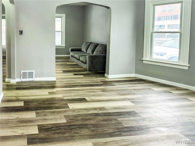 unfurnished room featuring arched walkways, visible vents, baseboards, and wood finished floors