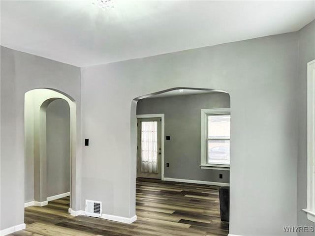 unfurnished room featuring baseboards, visible vents, arched walkways, and wood finished floors