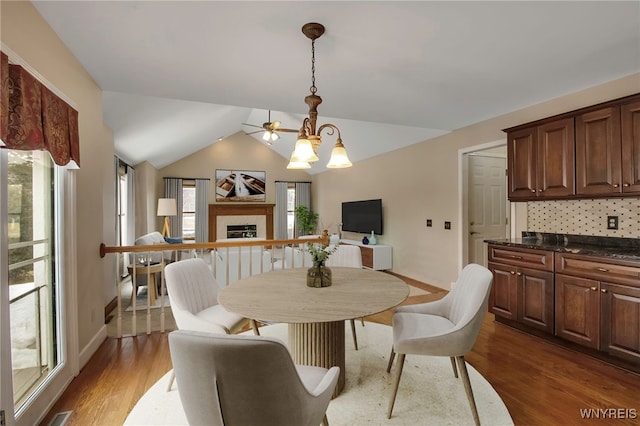 dining room featuring vaulted ceiling, dark wood-style flooring, a fireplace, and a healthy amount of sunlight