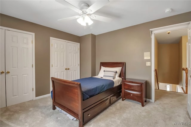 bedroom featuring light carpet, ceiling fan, baseboards, and multiple closets