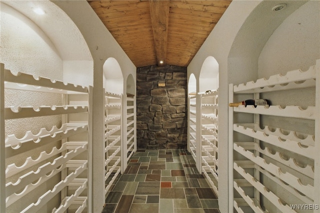 wine room featuring vaulted ceiling with beams, stone finish flooring, and wood ceiling