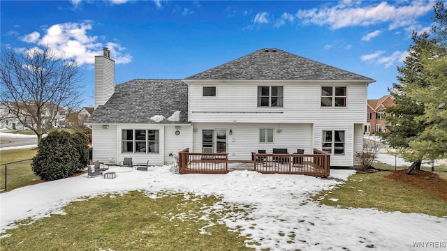 snow covered back of property with a chimney, fence, a deck, and a lawn