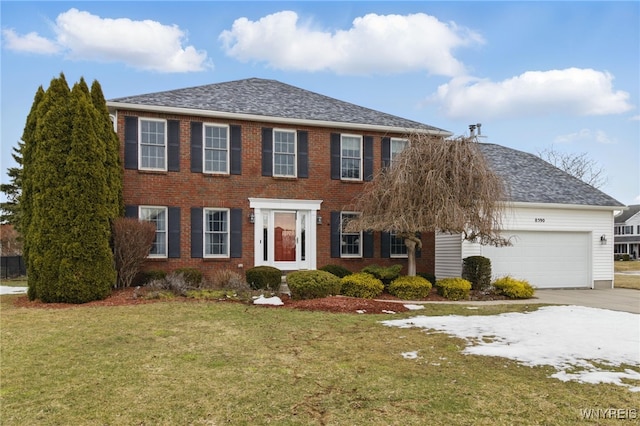 colonial house with brick siding, roof with shingles, concrete driveway, an attached garage, and a front yard