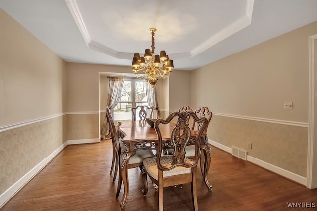 dining area with a tray ceiling, wood finished floors, visible vents, and wallpapered walls