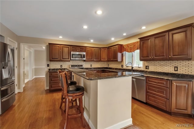 kitchen featuring tasteful backsplash, a breakfast bar area, stainless steel appliances, light wood-type flooring, and a sink