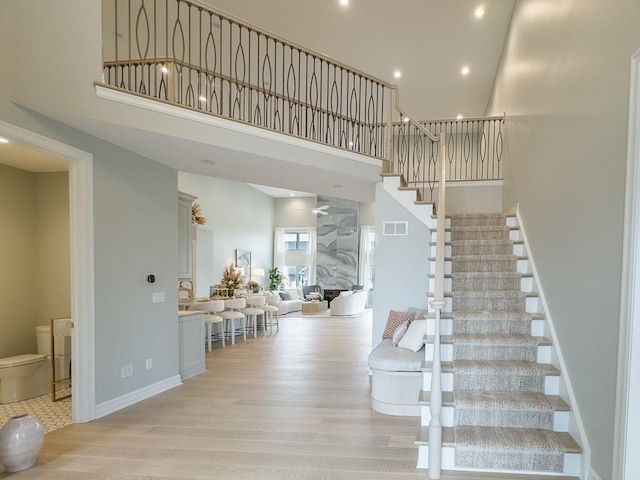 stairway featuring recessed lighting, a towering ceiling, baseboards, and wood finished floors