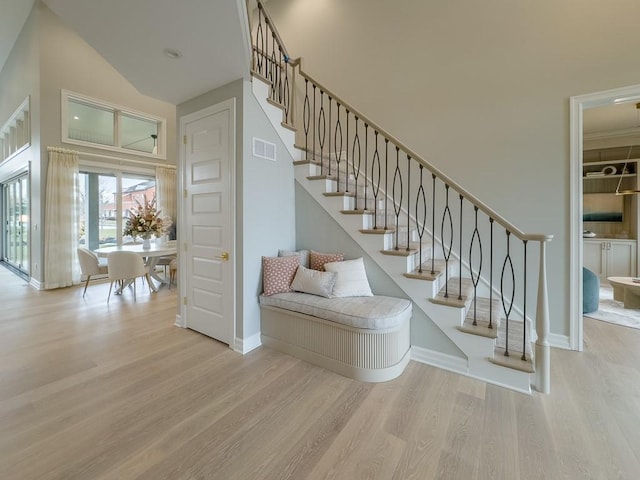 staircase with a high ceiling, wood finished floors, visible vents, and baseboards