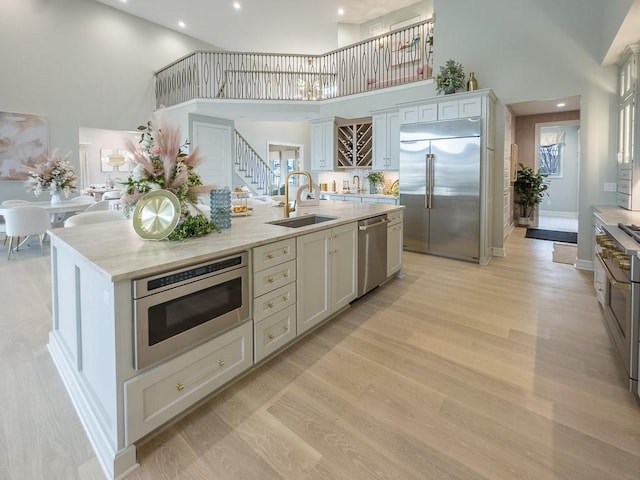 kitchen with built in appliances, a high ceiling, a sink, and light wood-style flooring