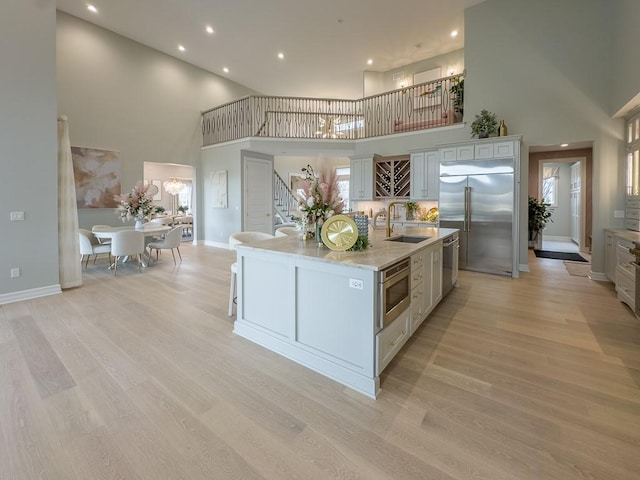 kitchen featuring light wood-type flooring, a kitchen island with sink, a sink, and built in appliances