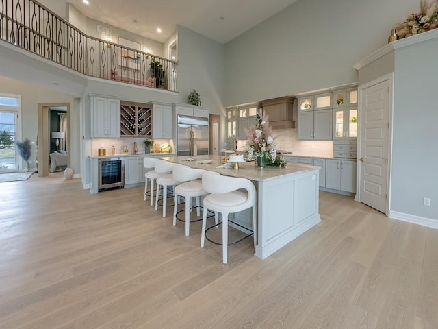 kitchen featuring wine cooler, light countertops, a large island with sink, light wood-style floors, and built in fridge