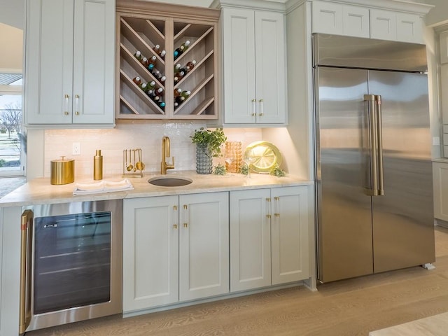 bar with tasteful backsplash, wine cooler, light wood-type flooring, a sink, and built in fridge