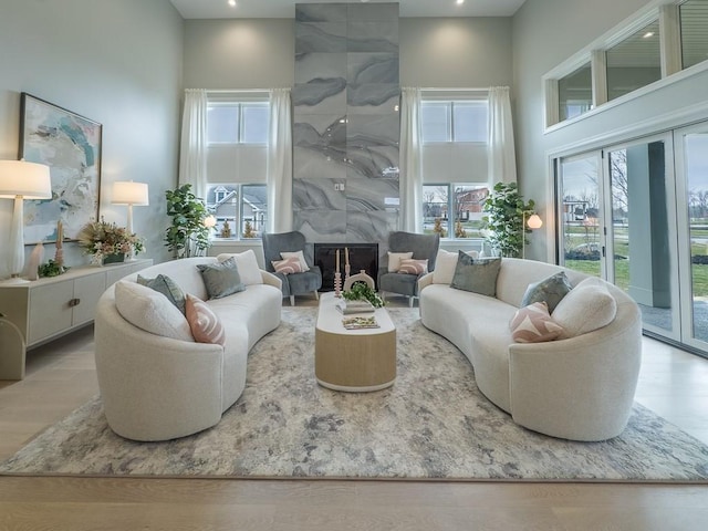 living room featuring a wealth of natural light, a premium fireplace, wood finished floors, and a towering ceiling